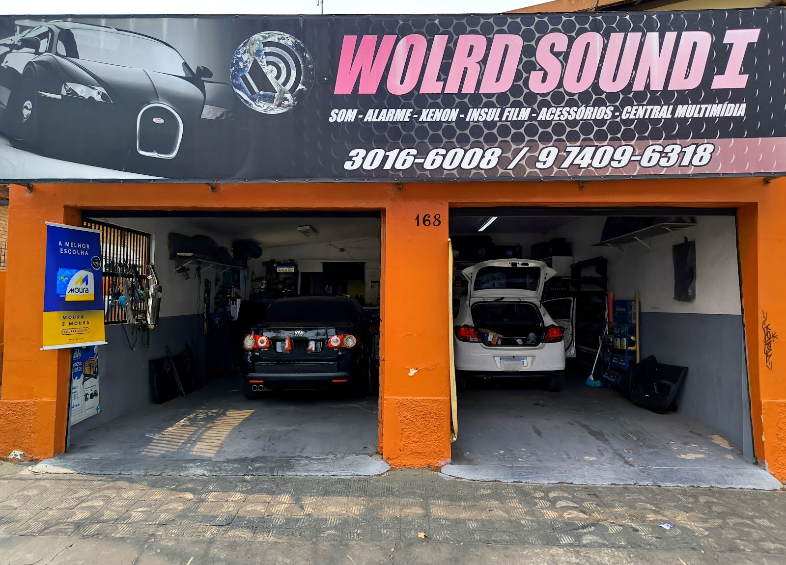 Fachada laranja da World Sound 1 com letreiro preto e dois boxes de atendimento com carros dentro