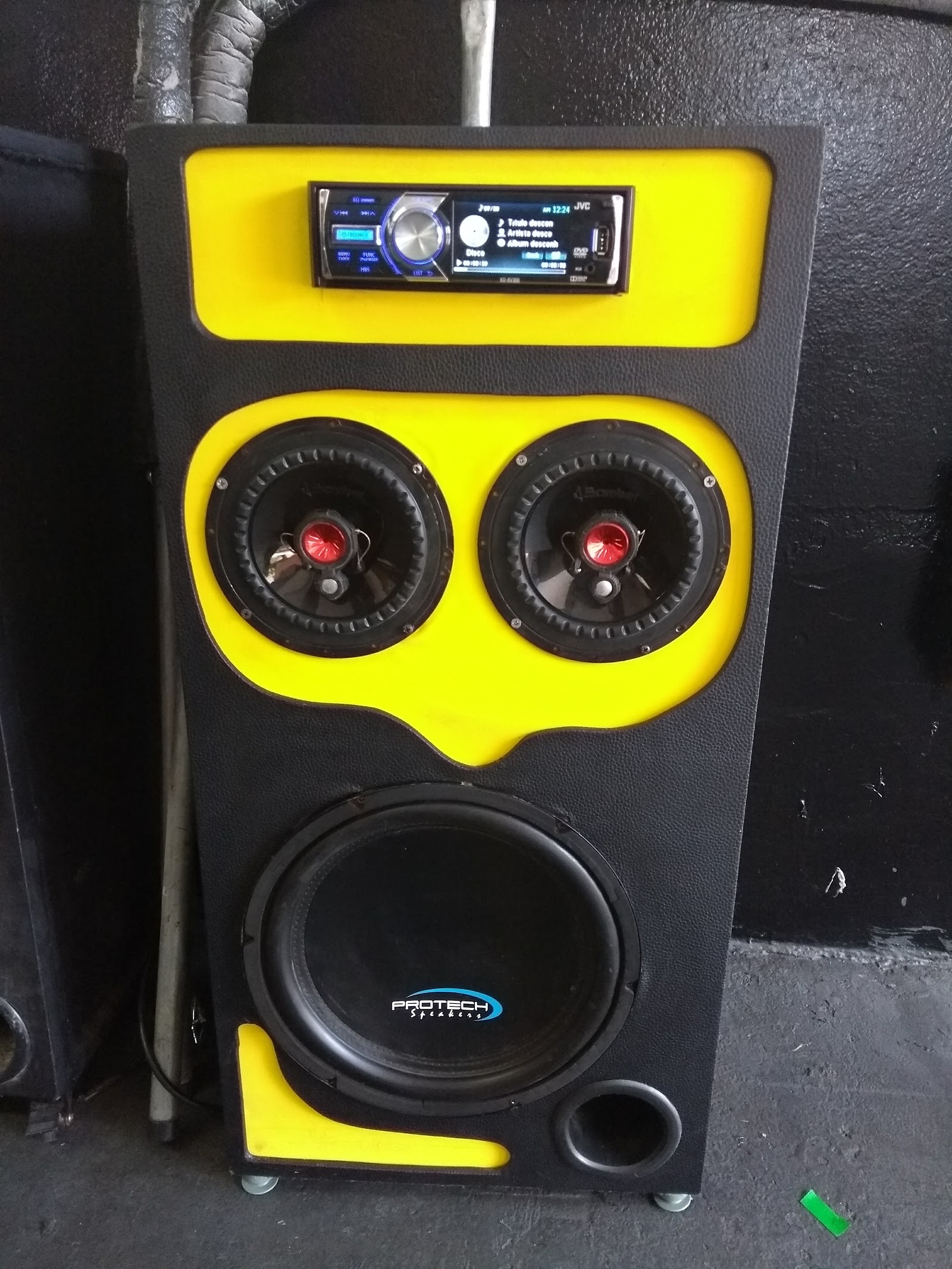 Caixa de som preta e amarela com player no topo, dois alto-falantes e um subwoofer