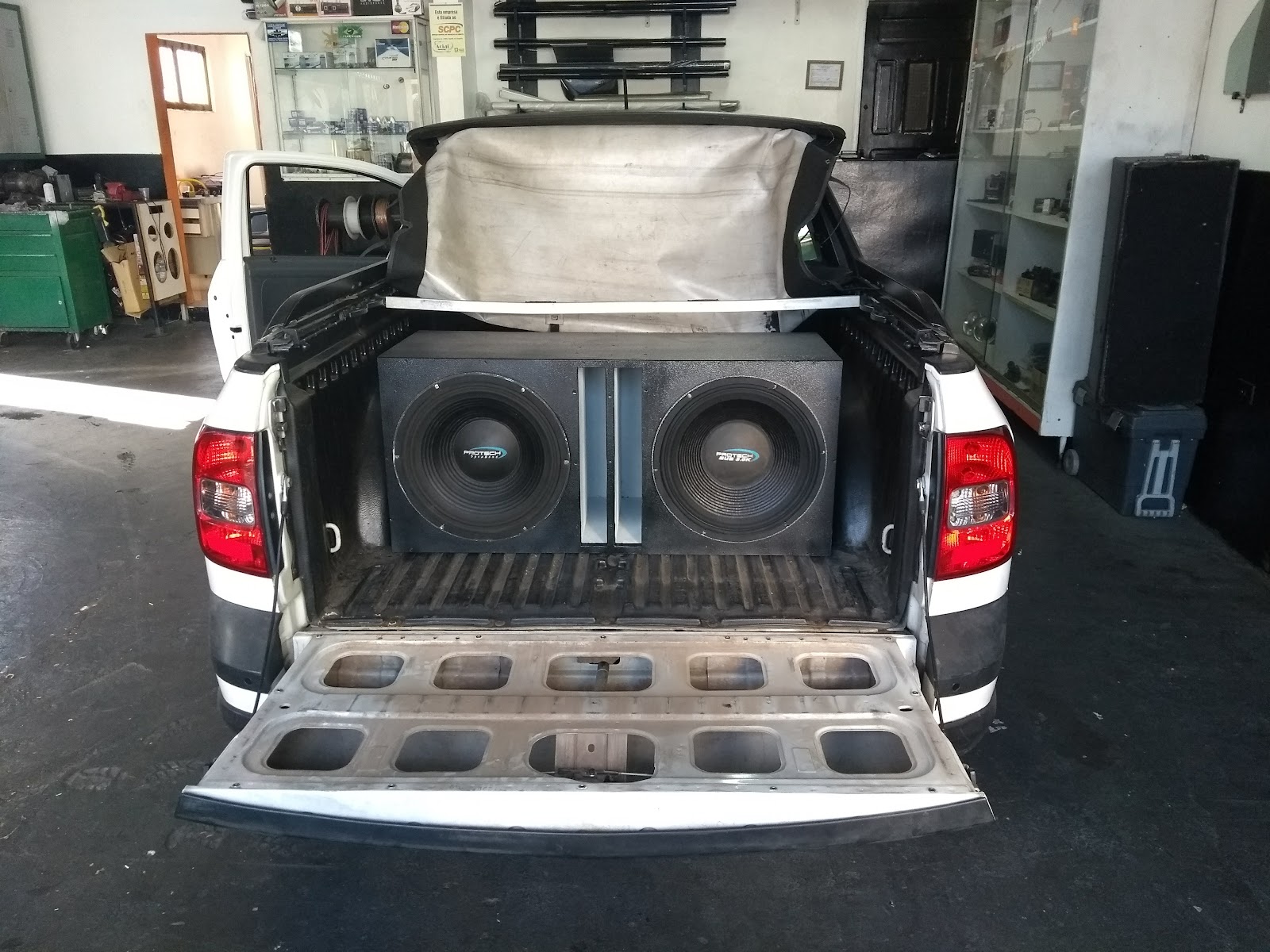 Caçamba de picape branca com caixa de dois subwoofers instalada, dentro da loja